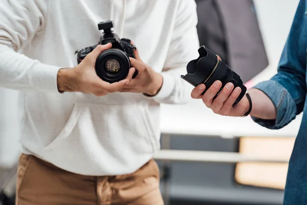 Vue recadrée du photographe tenant un appareil photo numérique près du directeur artistique avec objectif de l'appareil photo — Photo de stock