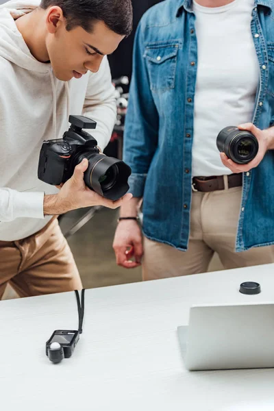 Vista recortada del director de arte sosteniendo lente de foto cerca de fotógrafo guapo - foto de stock