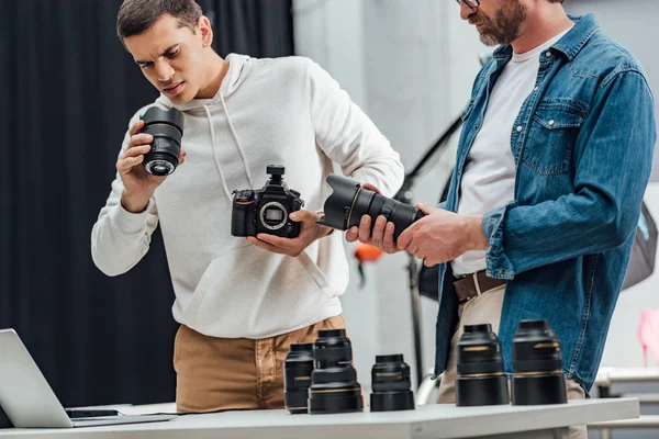 Cropped view of bearded art director holding photo lens near photographer — Stock Photo