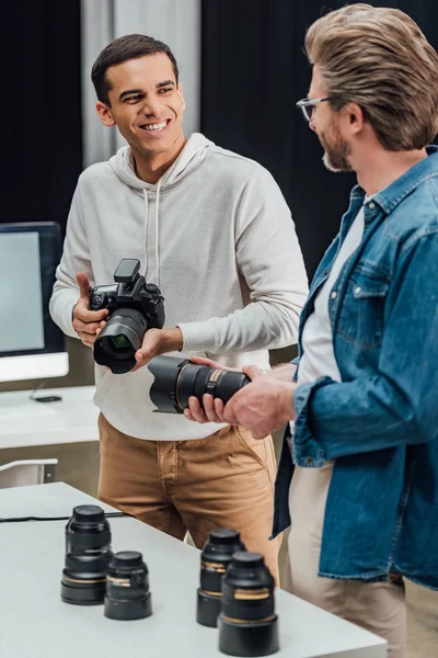 Director creativo barbudo sosteniendo lente de foto cerca fotógrafo feliz - foto de stock