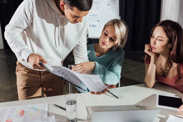 Handsome assistant holding contract near art director and coworkers — Stock Photo