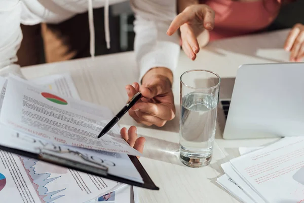 Abgeschnittene Ansicht des Art Directors, der mit dem Finger auf Klemmbrett in der Nähe seines Assistenten zeigt — Stockfoto