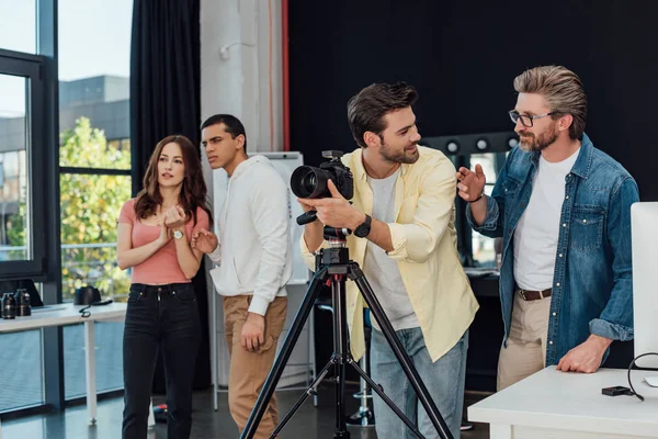 Fotógrafo tocando cámara digital cerca de director de arte en gafas y asistentes - foto de stock