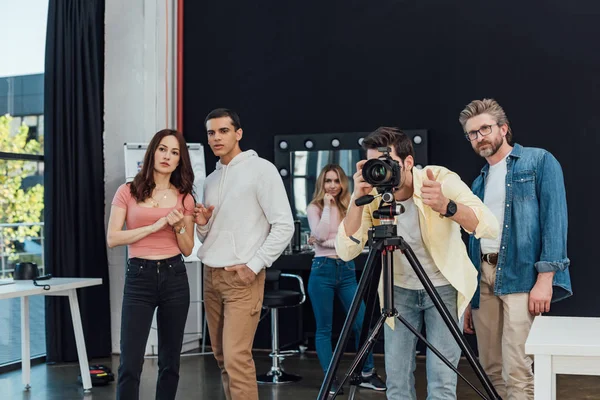 Fotógrafo tomando fotos cerca de director de arte en gafas y mostrando el pulgar hacia arriba - foto de stock