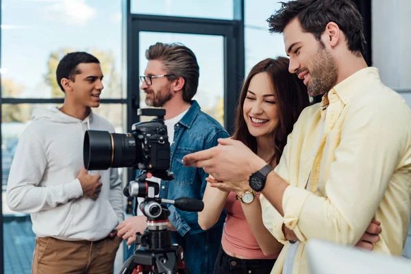 Selective focus of cheerful coworkers standing near digital camera — Stock Photo