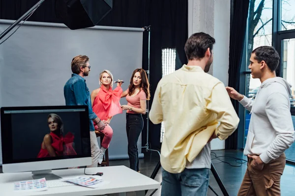 Selective focus of art director standing near makeup artist applying decorative cosmetics on model in photo studio — Stock Photo