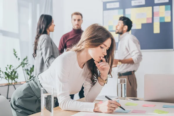 Selective focus of pensive scrum master holding pen near coworkers — Stock Photo