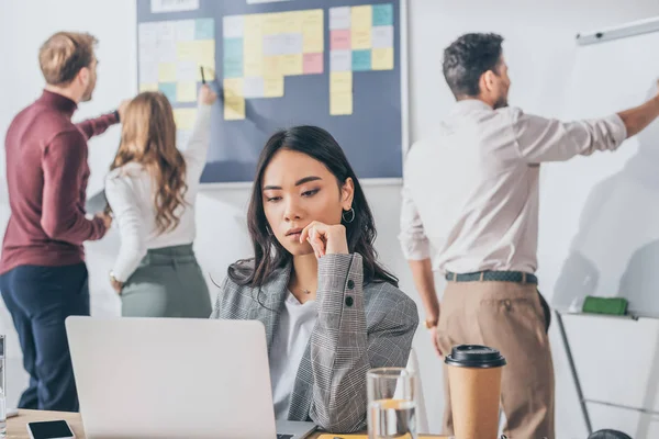 Selective focus of attractive asian businesswoman looking at laptop — Stock Photo