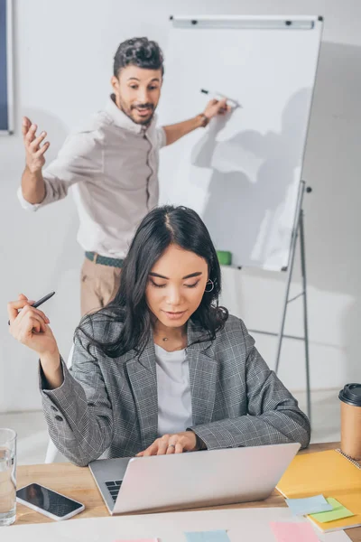 Selective focus of asian scrum master using laptop near mixed race man — Stock Photo