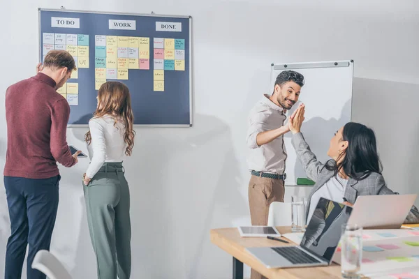 Feliz mixto la raza hombre dando alto cinco a asiático businesswoman cerca scrum maestros - foto de stock