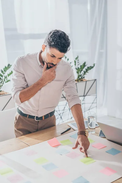 Pensive mixed race scrum master pointing with finger at blank sticky note — Stock Photo