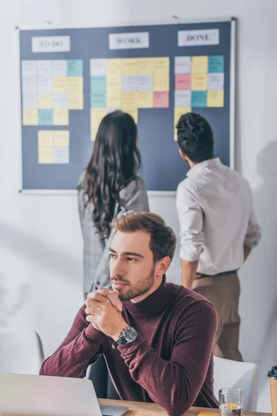 Enfoque selectivo de maestro de scrum guapo con las manos apretadas cerca de compañeros de trabajo - foto de stock