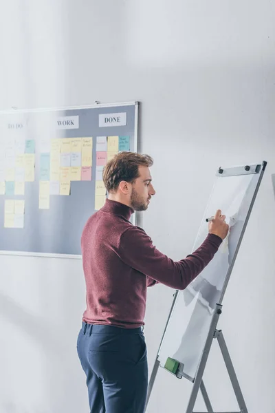 Side view of handsome scrum master writing on flipchart — Stock Photo