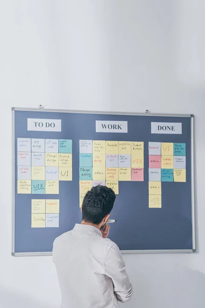 Back view of scrum master standing near board with sticky notes and letters — Stock Photo