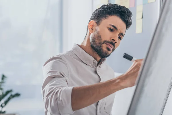 Selective focus of handsome mixed race scrum master writing on flipchart — Stock Photo