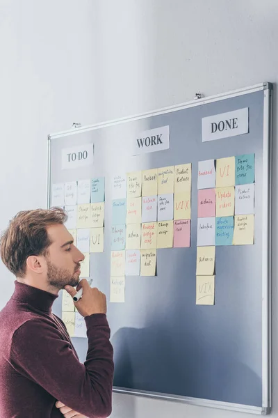 Seitenansicht eines gutaussehenden Gedrängemeisters, der in Brettnähe mit klebrigen Zetteln und Buchstaben denkt — Stockfoto