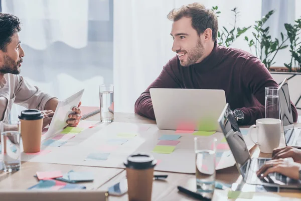 Enfoque selectivo de hombre de negocios multicultural hablando cerca de compañero de trabajo y gadgets - foto de stock