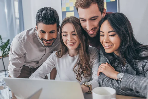 Homens de negócios multiculturais sorridentes e mulheres de negócios olhando para laptop no escritório — Fotografia de Stock