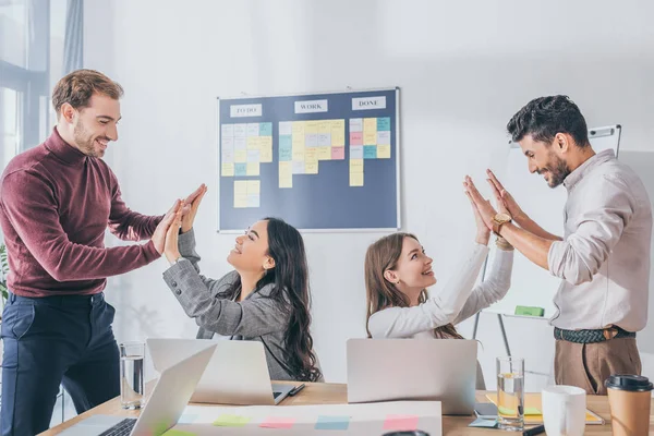 Cheerful multicultural businesswomen and businessmen giving high five in office — Stock Photo