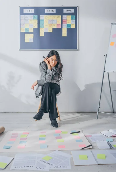 Schöne asiatische Gedränge Meister sitzt auf Stuhl und schaut auf klebrige Notizen — Stockfoto