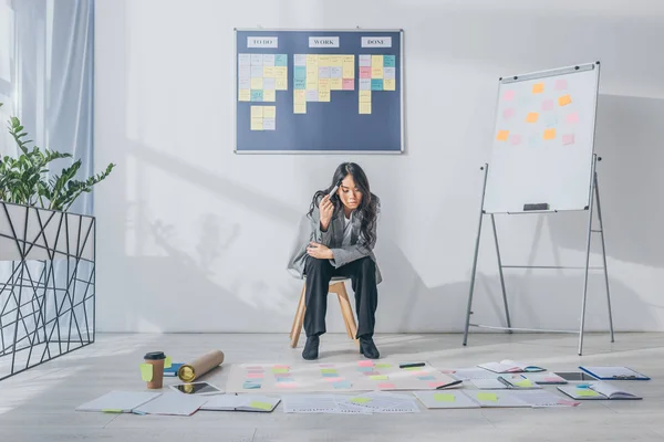 Pensive asian scrum master sitting on chair near gadgets and sticky notes — Stock Photo