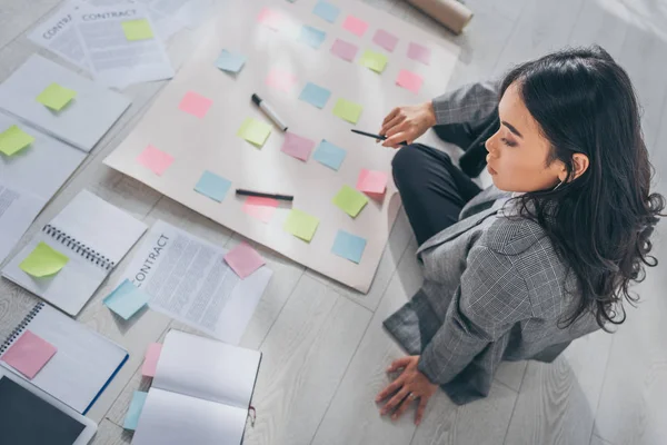 Overhead view of attractive asian scrum master sitting on floor and holding pen near contract — Stock Photo