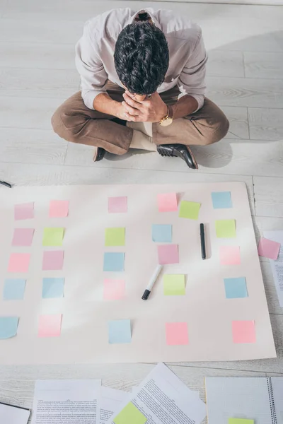 Top view of mixed race scrum master sitting on floor near sticky notes — Stock Photo