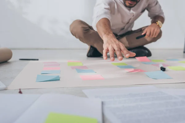 Cropped view of mixed race businessman sitting with outstretched hand near sticky notes on floor — Stock Photo