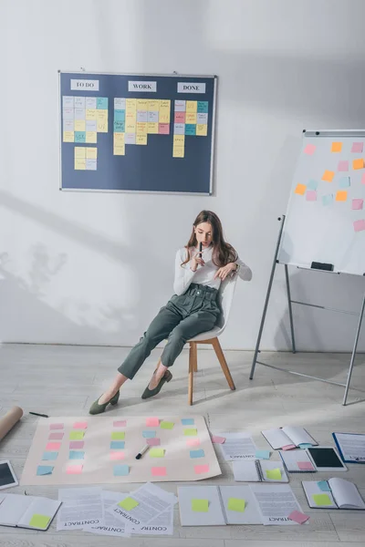 Pensive business woman sitting on chair near sticky notes on floor — стоковое фото