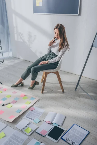 Jolie femme d'affaires assise sur une chaise près de notes collantes sur le sol — Photo de stock