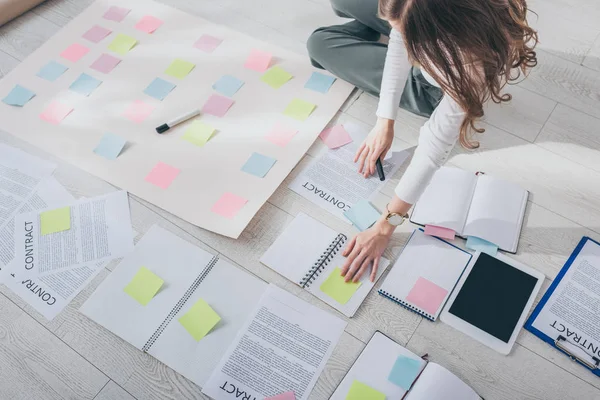 Vista recortada de la mujer de negocios sentada en el suelo cerca de la tableta digital con pantalla en blanco y notas adhesivas - foto de stock