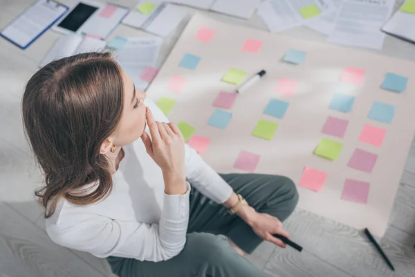 Vista aérea del maestro de scrum reflexivo mirando notas adhesivas en el suelo - foto de stock