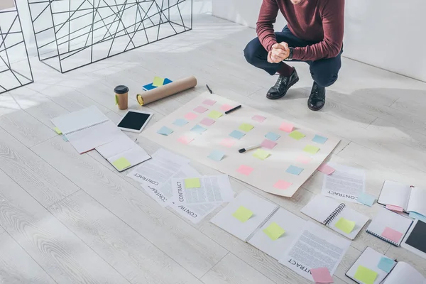 Cropped view of scrum master sitting with clenched hands near documents and gadgets on floor — Stock Photo