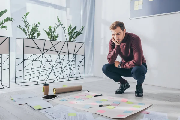 Schöner Gedrängemeister, der neben Dokumenten und Gerät auf dem Fußboden sitzt — Stockfoto