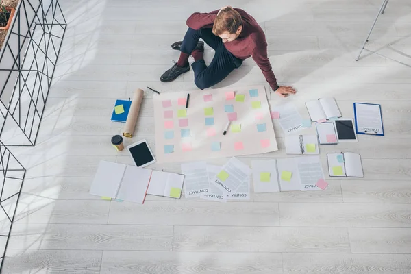 Top view of scrum master looking at sticky notes while sitting on floor — Stock Photo