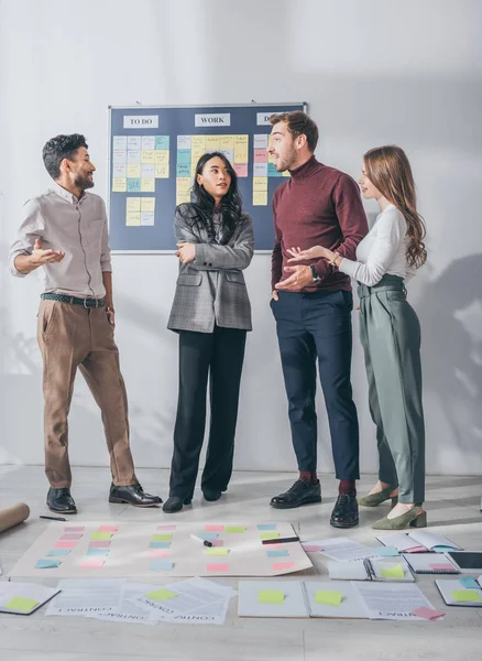 Multicultural scrum masters gesturing while talking near sticky notes on floor — Stock Photo