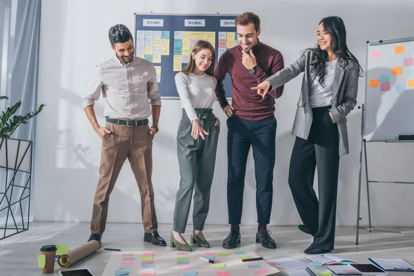 Happy multiccultural scrum masters looking at sticky notes on floor — стоковое фото