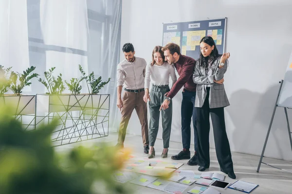 Selektiver Fokus glücklicher multikultureller Geschäftsleute, die mit den Fingern auf den Boden neben Geschäftsfrauen zeigen — Stockfoto