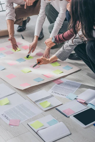 Vista recortada de los maestros scrum apuntando con los dedos al suelo con notas adhesivas cerca de documentos - foto de stock