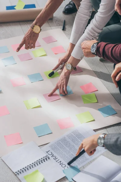 Cropped view of scrum masters pointing with fingers at floor with sticky notes near contract — Stock Photo