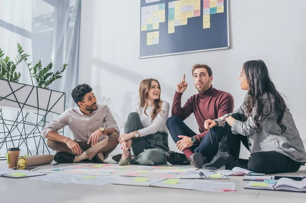 Happy multiccultural scrum masters sitting on floor and looking at man with idea — стоковое фото