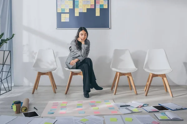 Beautiful asian scrum master sitting on chair near gadgets and sticky notes — Stock Photo
