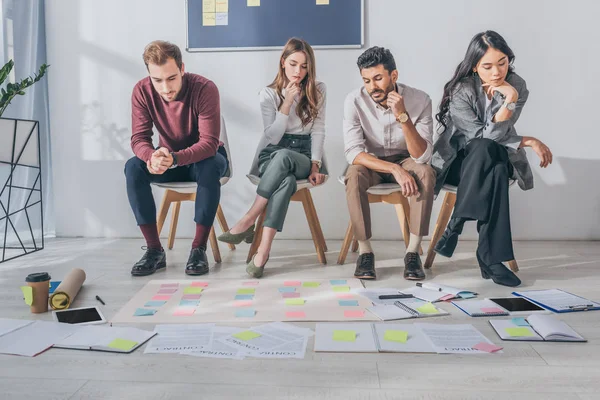 Pensive multicultural scrum masters sitting on chairs near sticky notes — Stock Photo