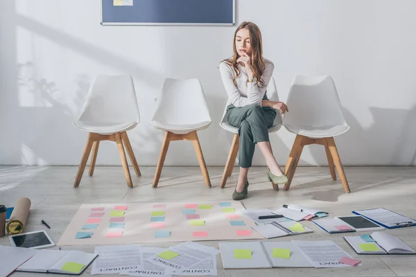 Attractive scrum master sitting on chair near sticky notes and gadgets on floor — Stock Photo