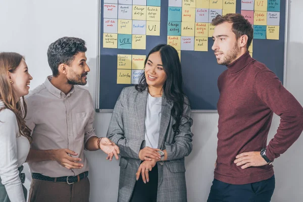 Alegres compañeros de trabajo multiculturales sonriendo en la oficina - foto de stock