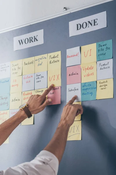 Vista recortada del hombre de negocios señalando con los dedos las notas adhesivas con letras en la oficina - foto de stock