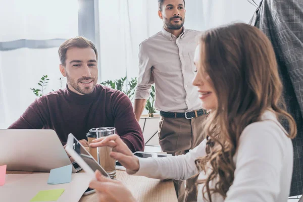 Selective focus of cheerful woman using digital tablet near multicultural coworkers — Stock Photo