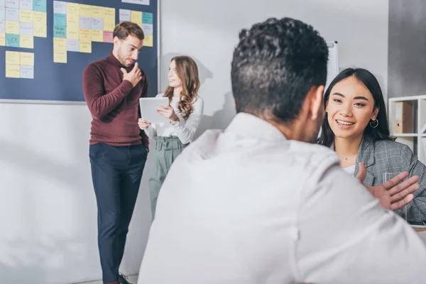 Selective focus of asian businesswoman looking at man near coworkers — Stock Photo