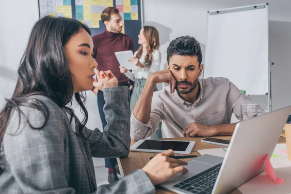 Selective focus of asian businesswoman using laptop near mixed race coworker — Stock Photo