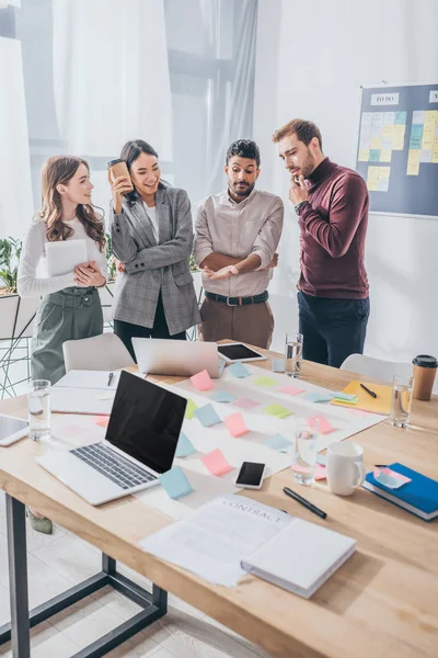 Multicultural businessmen and businesswomen near table with gadgets in office — Stock Photo